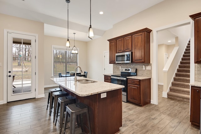 kitchen with backsplash, stainless steel appliances, a sink, and light wood finished floors