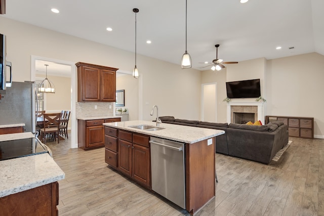 kitchen with decorative backsplash, a tile fireplace, stainless steel appliances, light wood-type flooring, and a sink