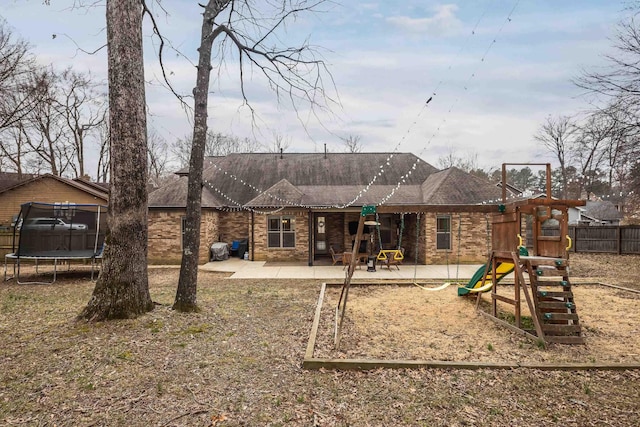 back of house with a playground, brick siding, fence, a trampoline, and a patio area