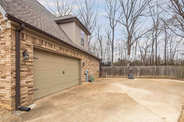 view of home's exterior featuring driveway, a garage, roof with shingles, fence, and brick siding