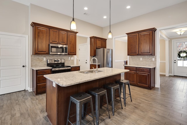 kitchen with appliances with stainless steel finishes, light wood-style floors, a sink, and a kitchen breakfast bar