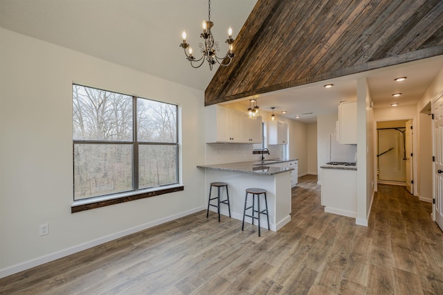 kitchen with a breakfast bar area, tasteful backsplash, white cabinets, wood finished floors, and a peninsula