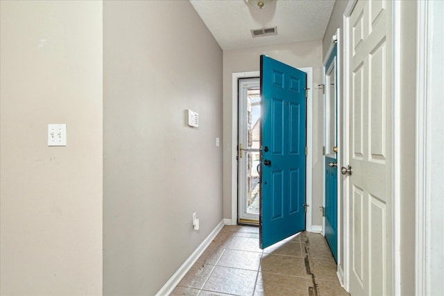 entryway featuring a textured ceiling, light tile patterned floors, visible vents, and baseboards