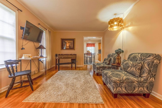 living area featuring baseboards, a chandelier, wood finished floors, and crown molding