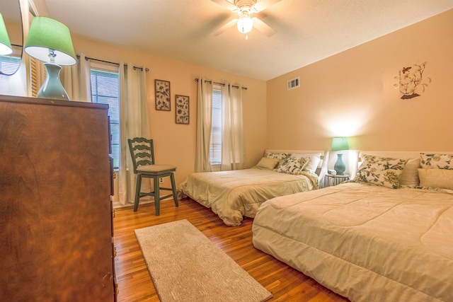 bedroom with ceiling fan, visible vents, and wood finished floors