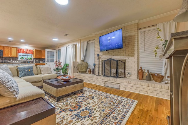 living area with recessed lighting, a fireplace, visible vents, ornamental molding, and light wood-type flooring