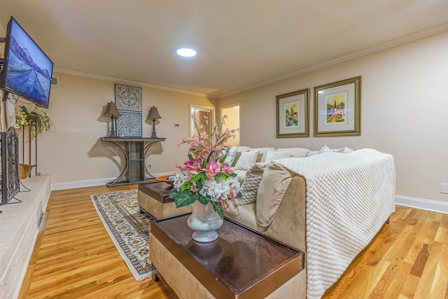 living room featuring a fireplace with raised hearth, crown molding, baseboards, and wood finished floors