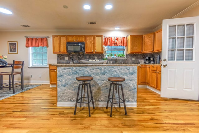 kitchen featuring black microwave, light wood finished floors, a kitchen bar, and visible vents