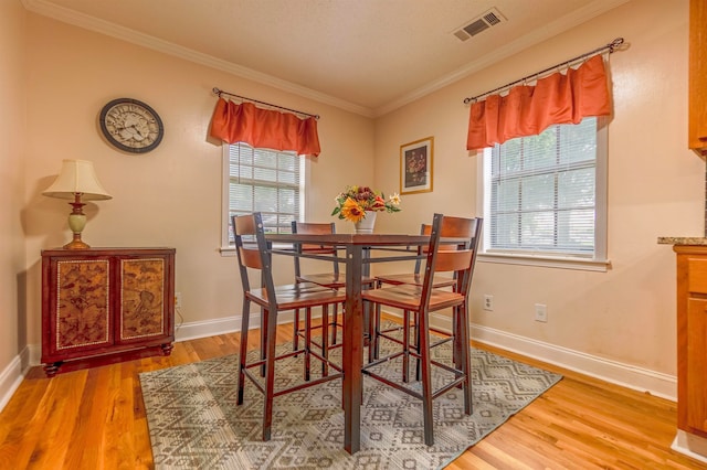 dining room with baseboards, wood finished floors, visible vents, and crown molding