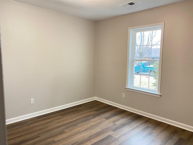 unfurnished room with visible vents, dark wood finished floors, a textured ceiling, and baseboards