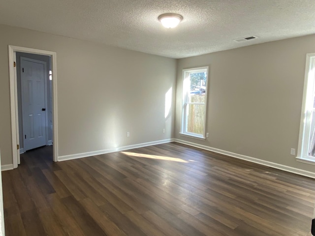 empty room featuring a textured ceiling, dark wood-style flooring, visible vents, and baseboards