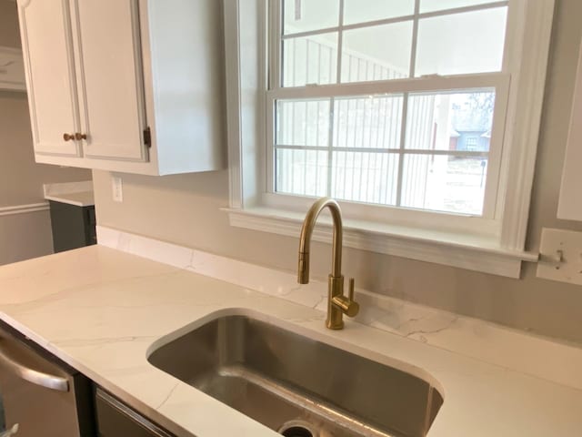 interior details featuring light stone countertops, white cabinets, a sink, and dishwasher