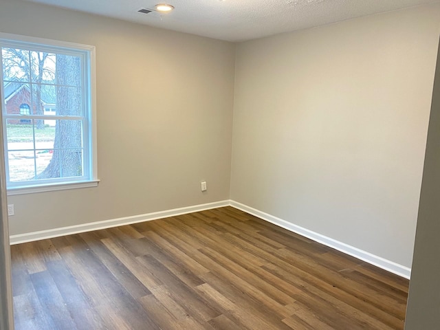 empty room featuring a textured ceiling, dark wood finished floors, visible vents, and baseboards