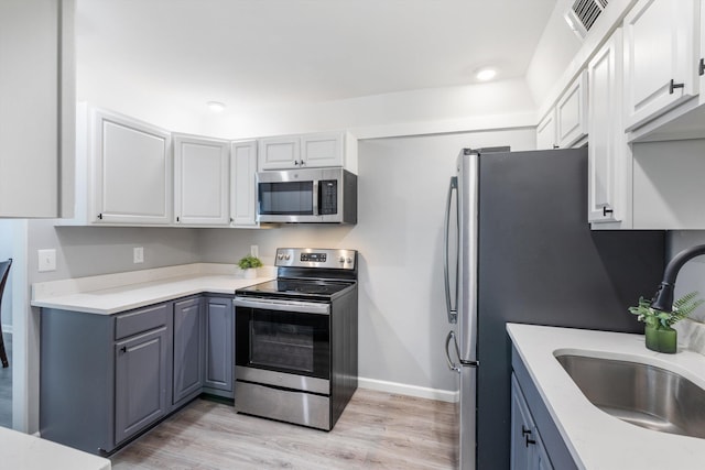 kitchen with light wood finished floors, light countertops, visible vents, appliances with stainless steel finishes, and a sink