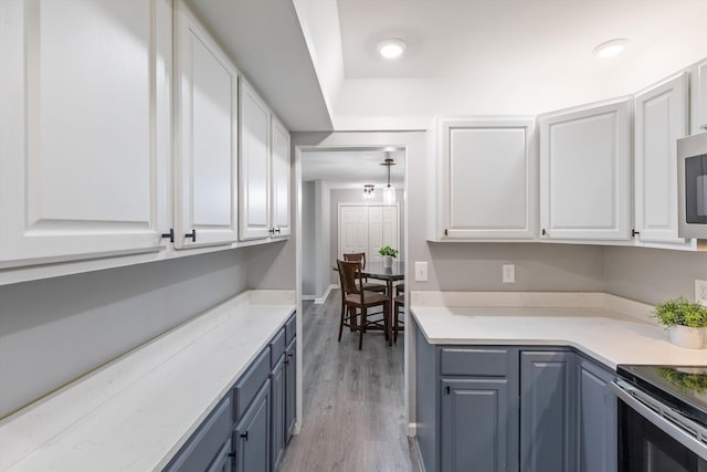 kitchen featuring baseboards, light wood-style floors, light countertops, white cabinets, and stainless steel microwave