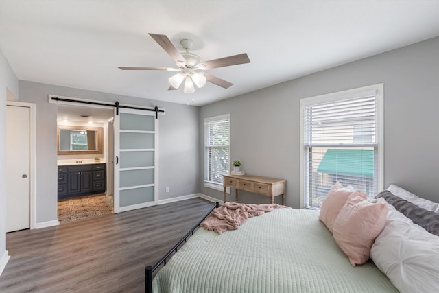 bedroom featuring a barn door, wood finished floors, a ceiling fan, baseboards, and ensuite bath