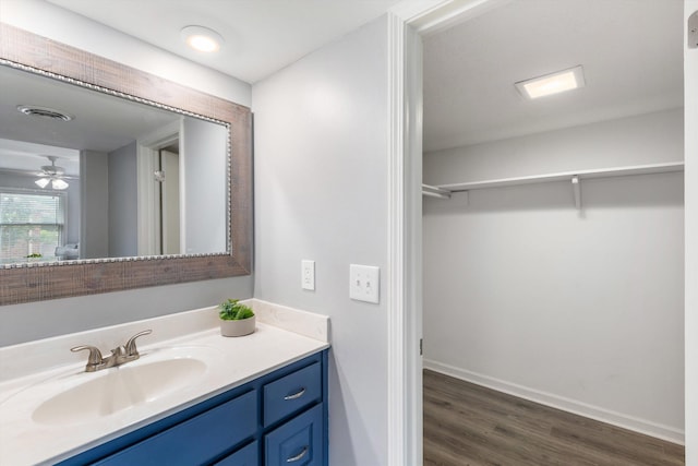 bathroom with baseboards, visible vents, wood finished floors, a walk in closet, and vanity