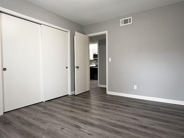 unfurnished bedroom featuring baseboards, visible vents, dark wood-style flooring, a textured ceiling, and a closet