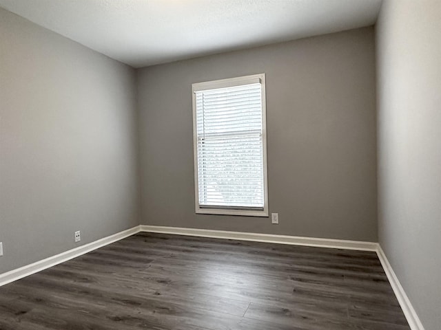 spare room featuring dark wood-type flooring and baseboards