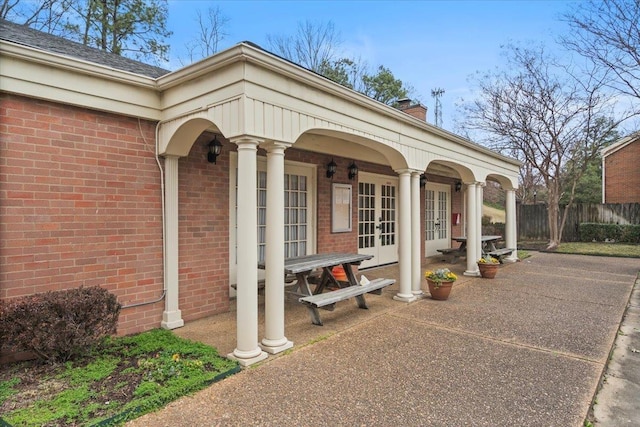 doorway to property with french doors, a chimney, fence, and brick siding