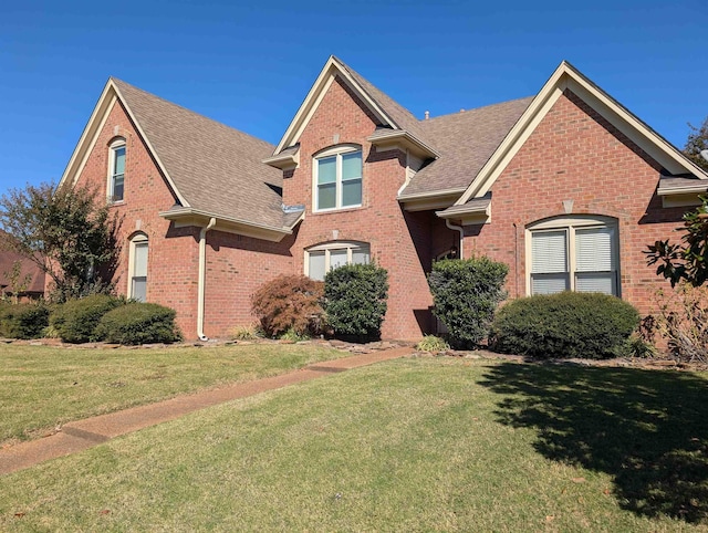 traditional home featuring a shingled roof, brick siding, and a front lawn