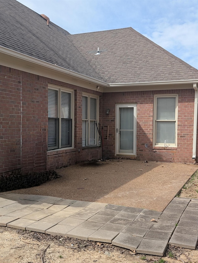 exterior space featuring a shingled roof and brick siding