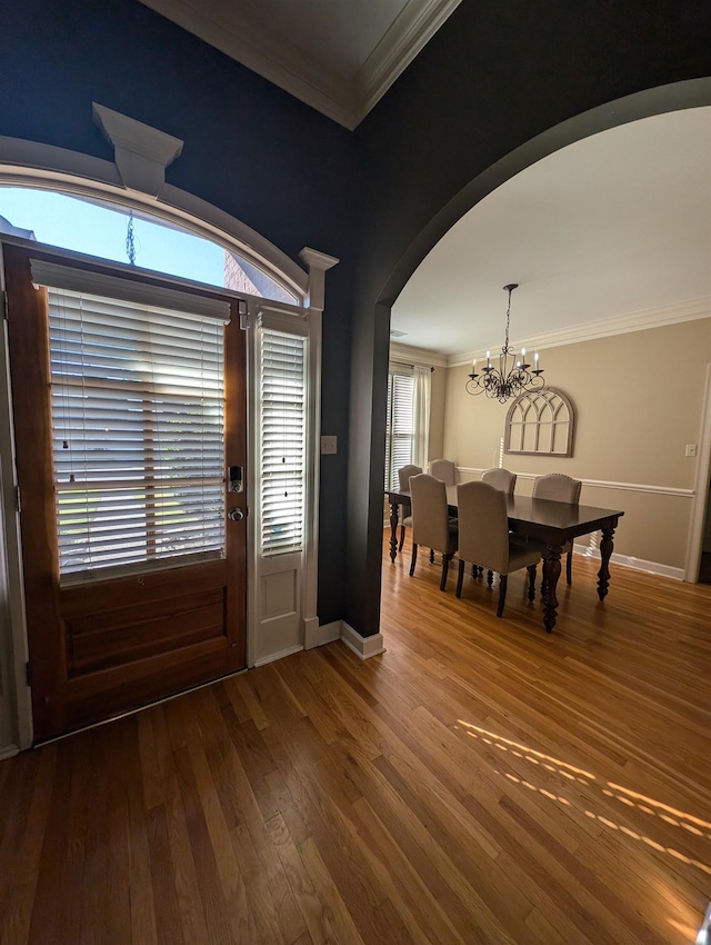 foyer entrance with baseboards, arched walkways, ornamental molding, wood finished floors, and a notable chandelier