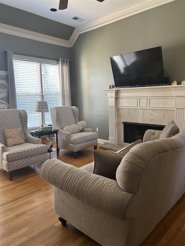 living room featuring a tile fireplace, wood finished floors, visible vents, a ceiling fan, and ornamental molding