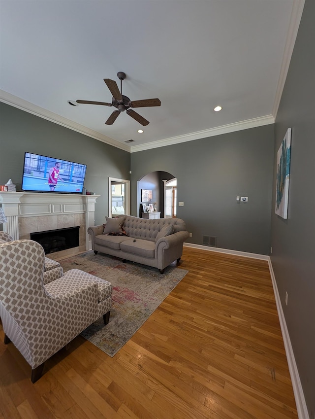 living area featuring arched walkways, a tile fireplace, wood finished floors, visible vents, and baseboards