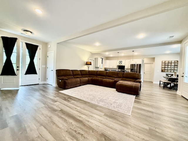 living room featuring light wood finished floors, visible vents, baseboards, and beam ceiling