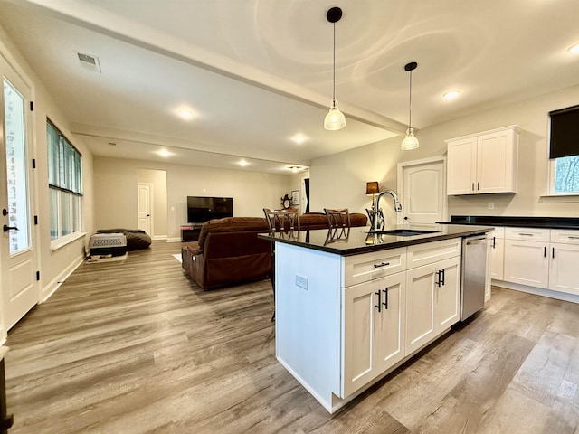 kitchen with dishwasher, dark countertops, a sink, and visible vents