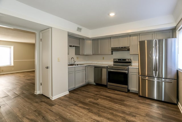 kitchen featuring gray cabinets, stainless steel appliances, light countertops, under cabinet range hood, and a sink