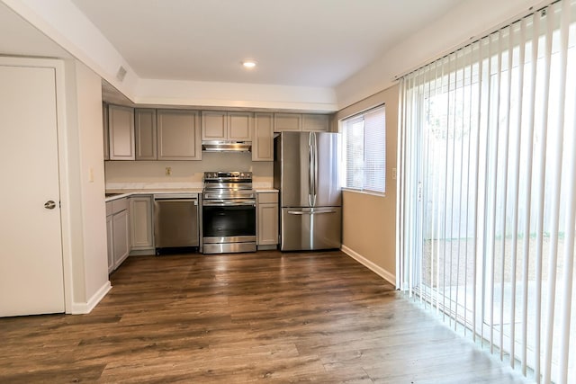 kitchen with under cabinet range hood, stainless steel appliances, light countertops, gray cabinets, and dark wood finished floors