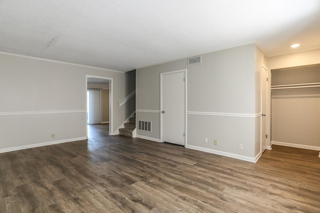 empty room with dark wood-type flooring, visible vents, baseboards, and stairs