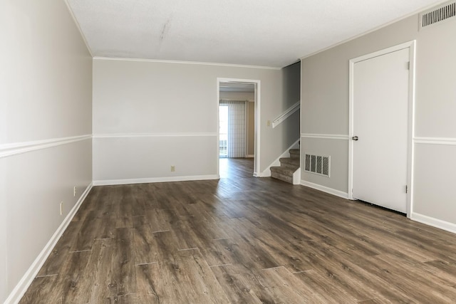 empty room featuring ornamental molding, stairway, wood finished floors, and visible vents