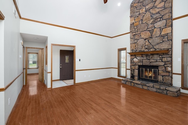 unfurnished living room with crown molding, a stone fireplace, wood finished floors, high vaulted ceiling, and baseboards