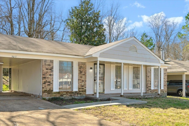 view of front of home featuring driveway, covered porch, a front lawn, a carport, and brick siding