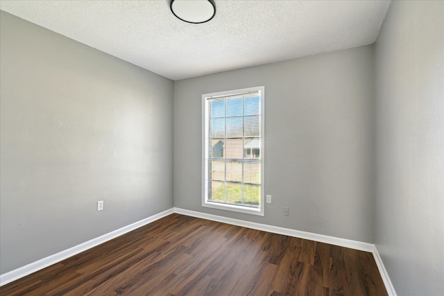 empty room with dark wood-type flooring, a textured ceiling, and baseboards