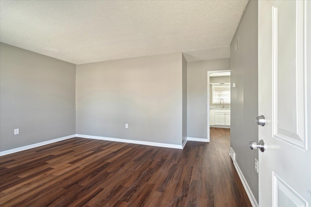 unfurnished room with dark wood-style flooring, a textured ceiling, and baseboards