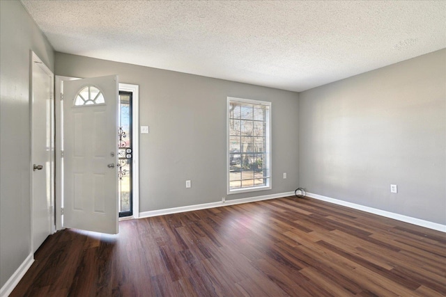 foyer entrance with dark wood-style flooring, a textured ceiling, and baseboards