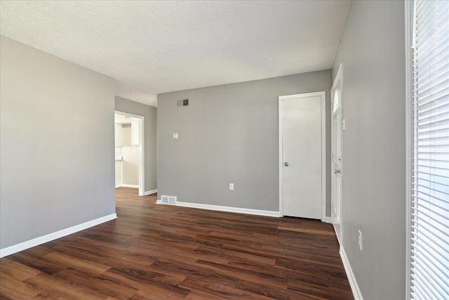 empty room with dark wood-style floors, visible vents, a textured ceiling, and baseboards