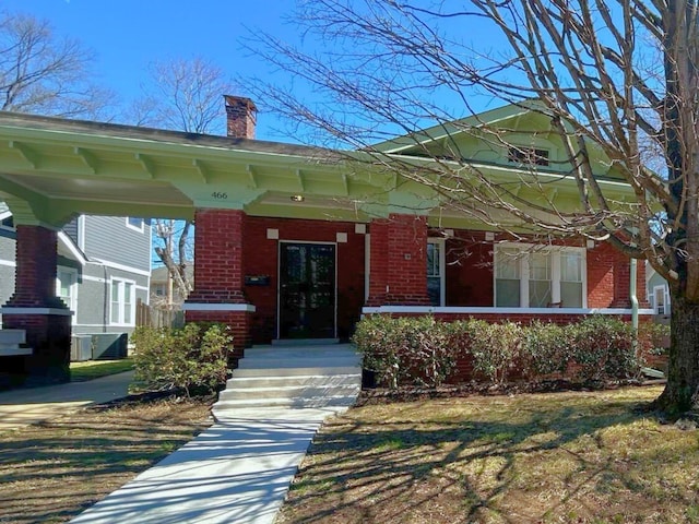 doorway to property with brick siding, a chimney, and a porch