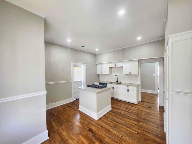 kitchen featuring white cabinets, decorative backsplash, a kitchen island, dark wood-style flooring, and a sink