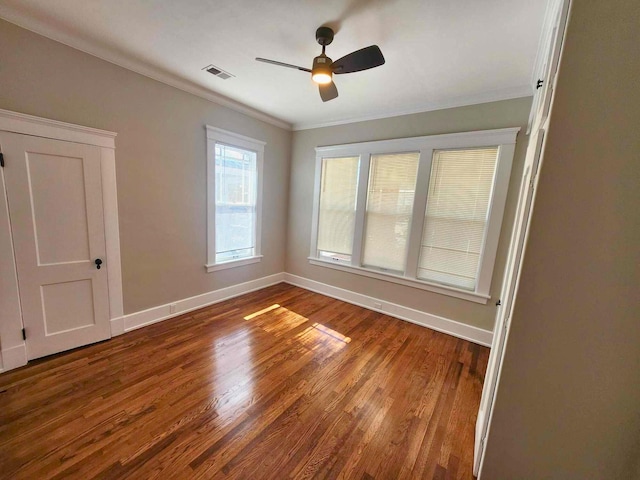 empty room with ceiling fan, wood finished floors, visible vents, baseboards, and ornamental molding