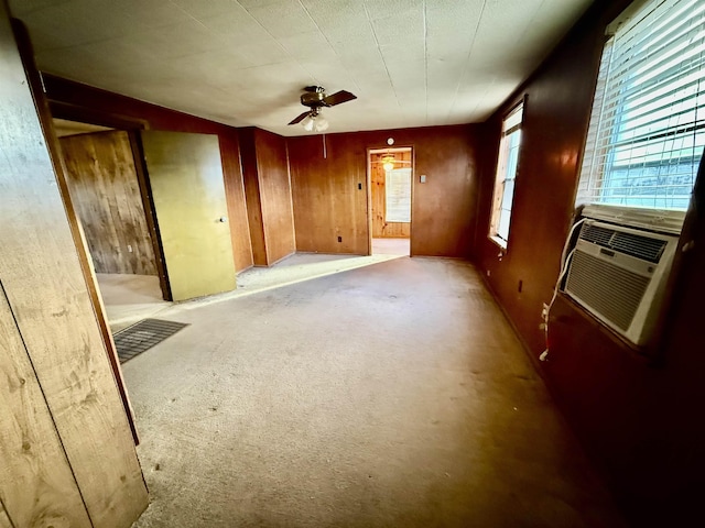 empty room featuring light carpet, wood walls, ceiling fan, and cooling unit