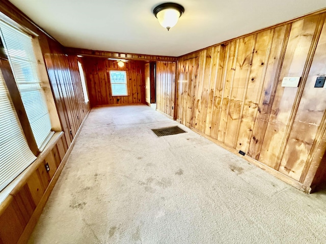 empty room featuring light carpet, wood walls, and visible vents