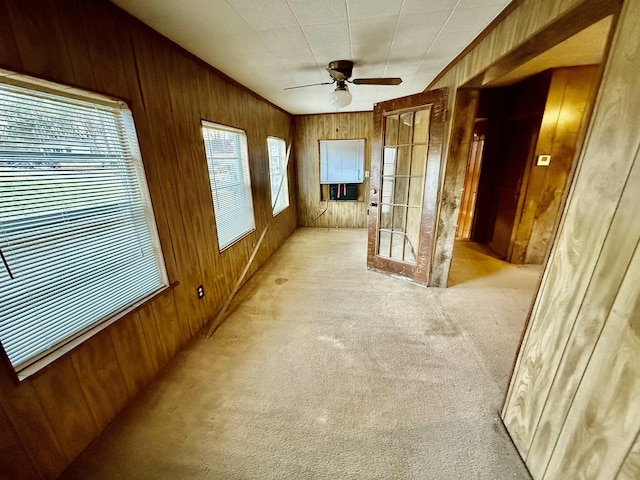 interior space with a ceiling fan, french doors, light colored carpet, and wooden walls