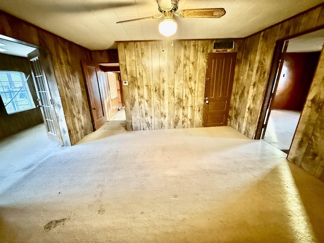 carpeted empty room with wood walls and a ceiling fan