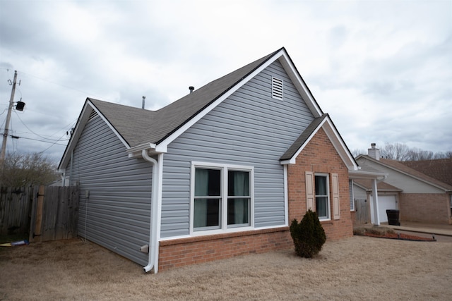 rear view of house featuring brick siding, fence, and roof with shingles