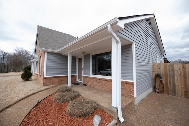 view of side of property with a shingled roof, fence, and brick siding